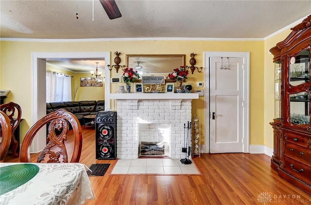 living room with a textured ceiling, light wood-style flooring, a ceiling fan, ornamental molding, and a brick fireplace