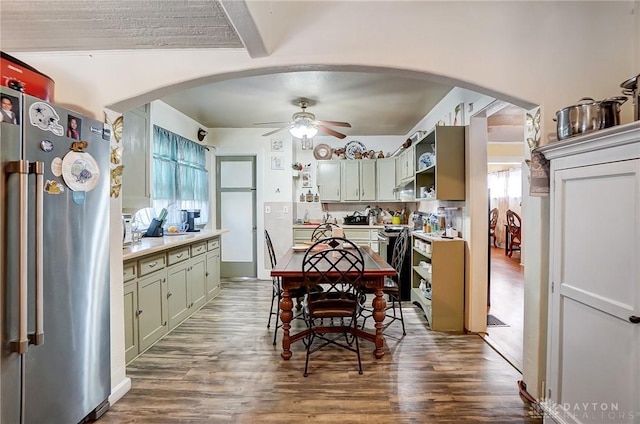 kitchen featuring arched walkways, open shelves, light countertops, appliances with stainless steel finishes, and green cabinetry