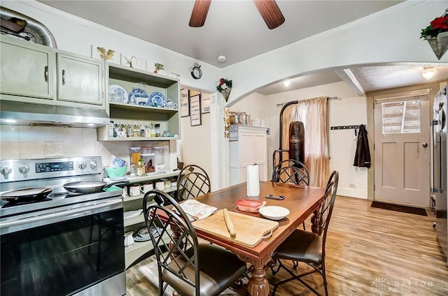 dining room with arched walkways, light wood finished floors, and a ceiling fan