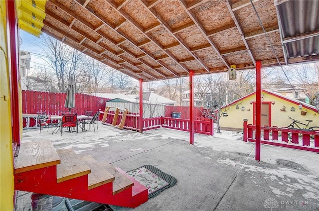 snow covered patio featuring a fenced backyard, an outbuilding, and outdoor dining space