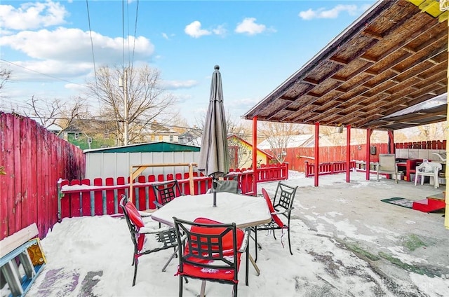 snow covered patio featuring a fenced backyard and outdoor dining area