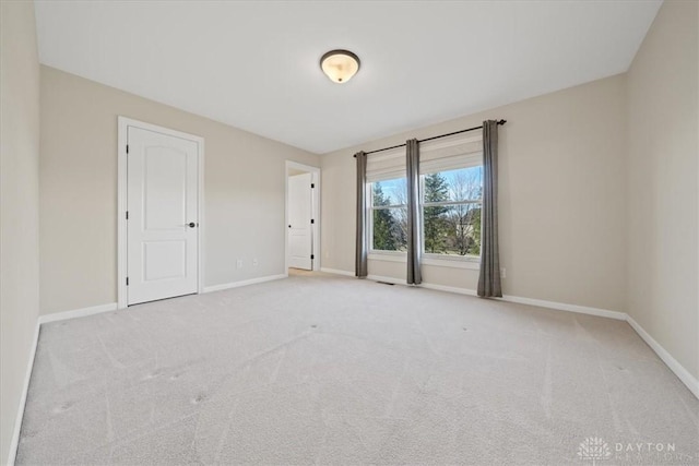 spare room with baseboards and light colored carpet