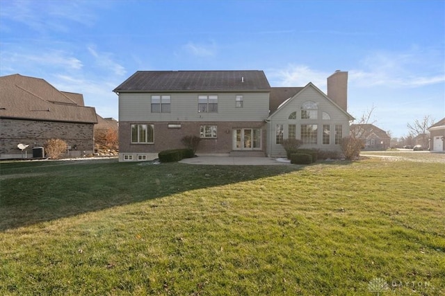 back of property featuring a chimney, a lawn, and a patio area