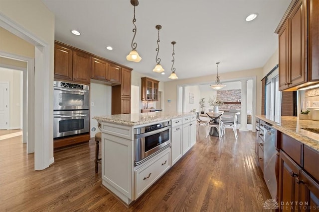 kitchen with glass insert cabinets, a center island, decorative light fixtures, stainless steel appliances, and white cabinetry