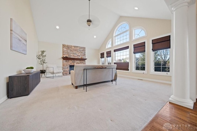 living area with high vaulted ceiling, a stone fireplace, decorative columns, and light colored carpet