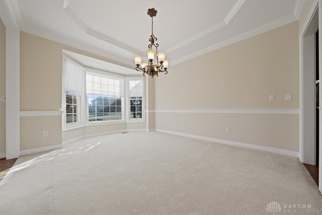 carpeted spare room featuring a notable chandelier, ornamental molding, a raised ceiling, and baseboards