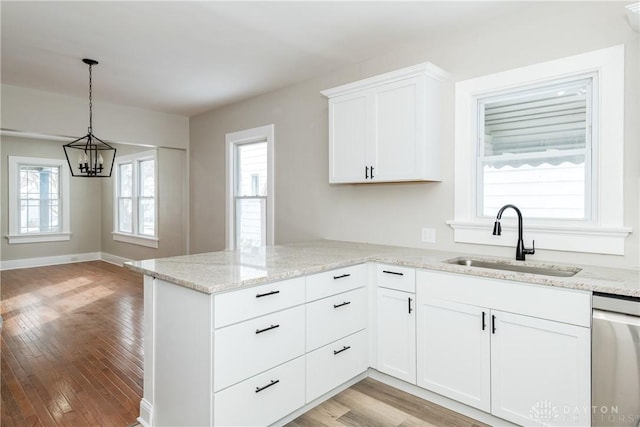 kitchen featuring white cabinets, decorative light fixtures, a sink, light wood-type flooring, and stainless steel dishwasher