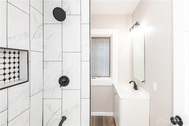 full bath featuring tiled shower, wood finished floors, vanity, and baseboards