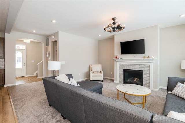 living area with arched walkways, recessed lighting, a brick fireplace, light wood-type flooring, and baseboards