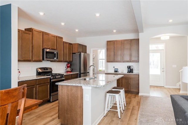 kitchen with a breakfast bar area, light wood-style flooring, appliances with stainless steel finishes, a kitchen island with sink, and a sink