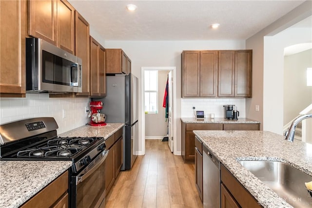 kitchen featuring appliances with stainless steel finishes, brown cabinetry, a sink, and light wood-style flooring