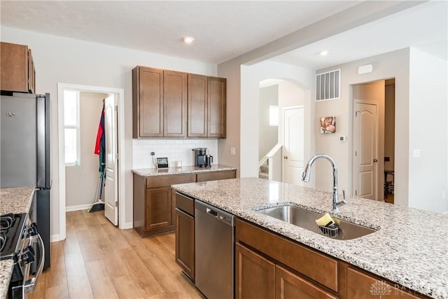 kitchen featuring visible vents, appliances with stainless steel finishes, light stone counters, light wood-style floors, and a sink