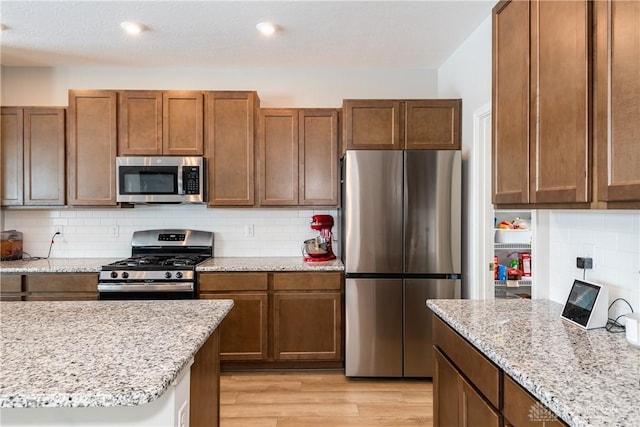 kitchen featuring appliances with stainless steel finishes, brown cabinetry, and light wood-style flooring