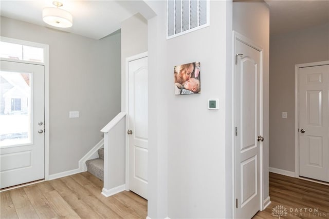 entrance foyer with light wood-type flooring, visible vents, baseboards, and stairs