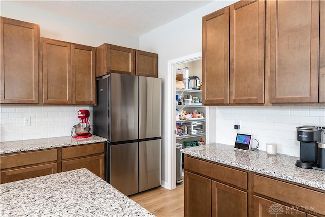 kitchen featuring brown cabinetry, freestanding refrigerator, and light stone counters