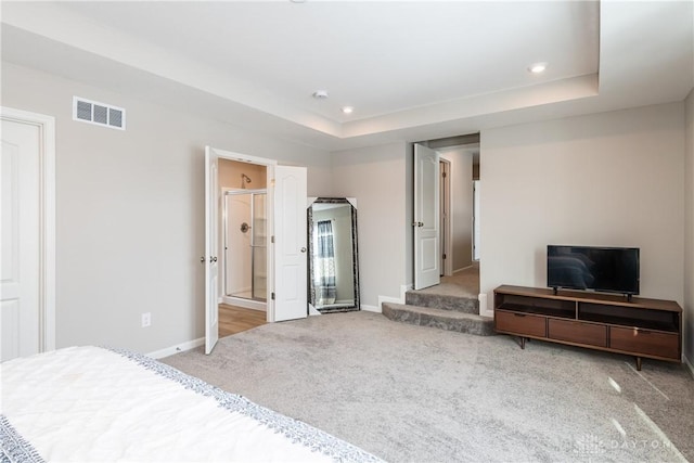 bedroom with a tray ceiling, visible vents, light carpet, and baseboards