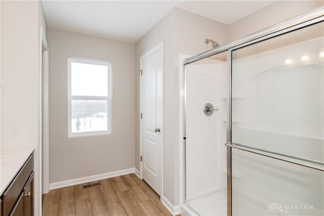 bathroom featuring wood finished floors, vanity, visible vents, baseboards, and a stall shower