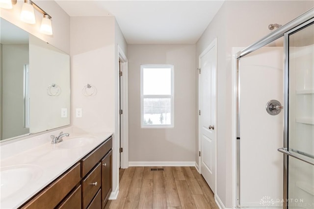 full bath with a shower with door, baseboards, a sink, and wood finished floors