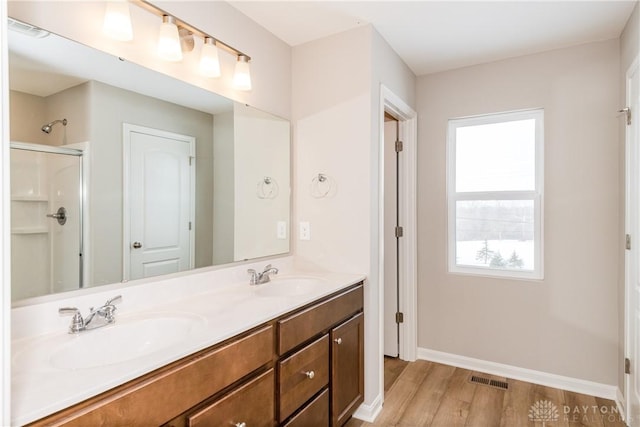 full bathroom featuring a shower with door, visible vents, a sink, and wood finished floors