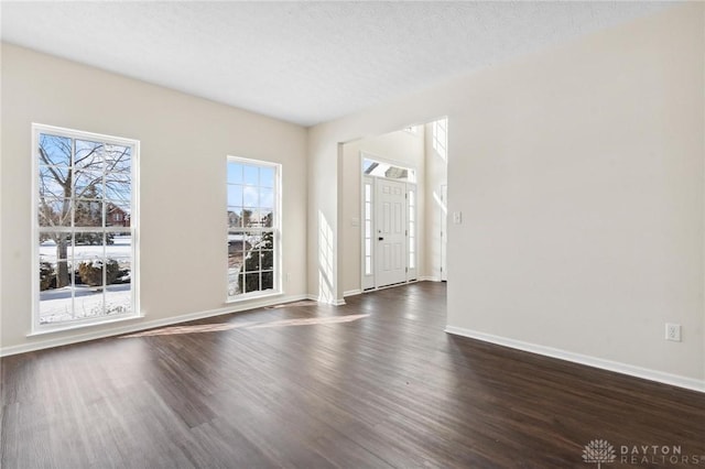 empty room with baseboards, dark wood-type flooring, and a textured ceiling