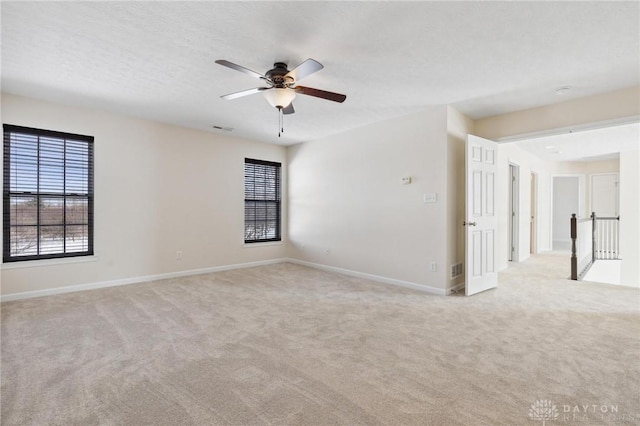 empty room with visible vents, a ceiling fan, a textured ceiling, baseboards, and light colored carpet