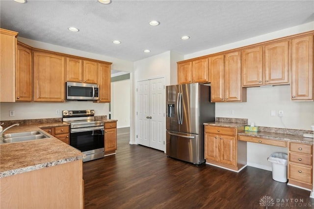 kitchen with built in study area, dark wood-type flooring, appliances with stainless steel finishes, and a sink