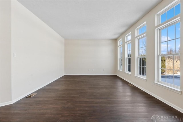 empty room with baseboards, visible vents, and dark wood-style flooring