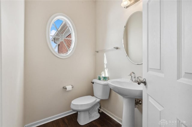 bathroom with toilet, wood finished floors, baseboards, and a sink