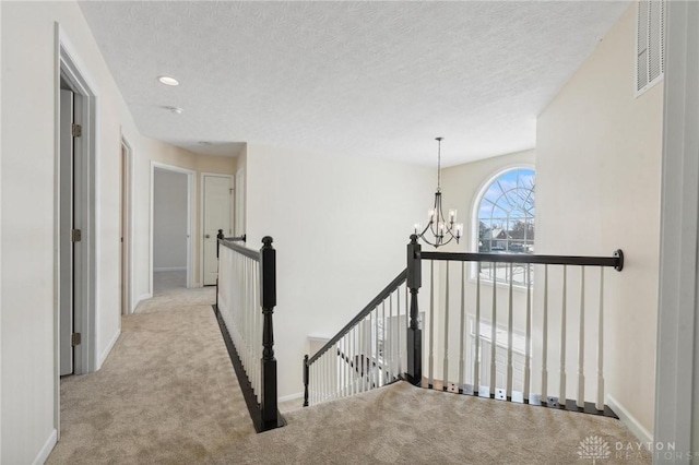 hall with visible vents, carpet, a chandelier, an upstairs landing, and a textured ceiling