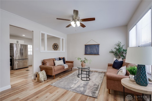 living area with baseboards, crown molding, light wood-style flooring, and a ceiling fan