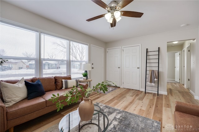 living area featuring light wood-style flooring, baseboards, and a ceiling fan