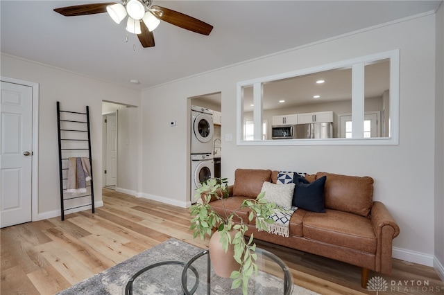 living area featuring baseboards, ceiling fan, light wood-type flooring, and stacked washer / drying machine