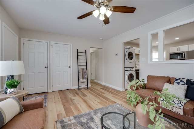 living room with light wood-style floors, baseboards, stacked washing maching and dryer, and a ceiling fan