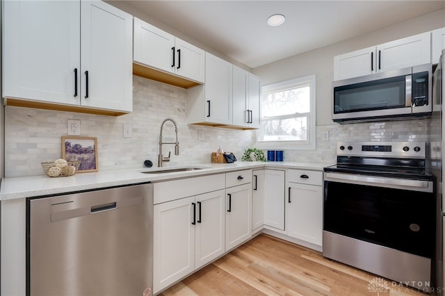 kitchen featuring light wood finished floors, white cabinets, decorative backsplash, stainless steel appliances, and a sink