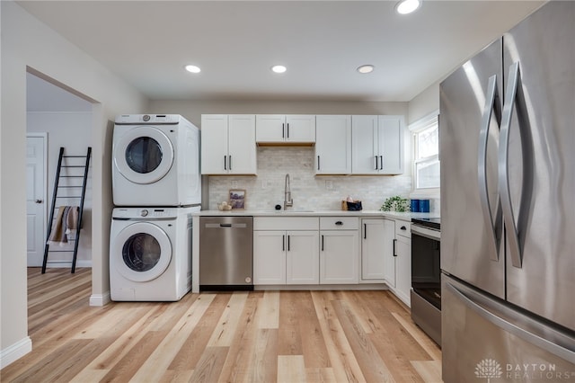 kitchen with a sink, white cabinetry, appliances with stainless steel finishes, and stacked washer / drying machine