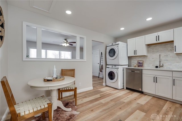 kitchen with light countertops, white cabinets, stainless steel dishwasher, and stacked washer and clothes dryer