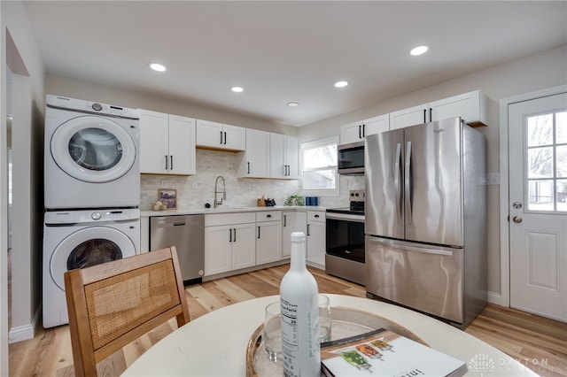 kitchen with stainless steel appliances, white cabinetry, light countertops, stacked washing maching and dryer, and tasteful backsplash