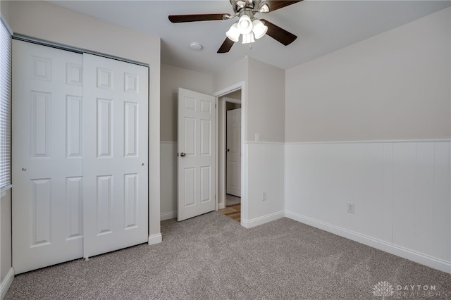 unfurnished bedroom with a ceiling fan, a closet, light carpet, and wainscoting