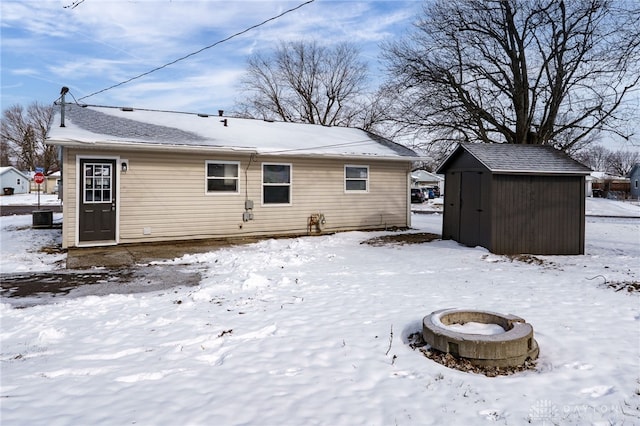 snow covered house with an outbuilding, cooling unit, a fire pit, and a storage shed