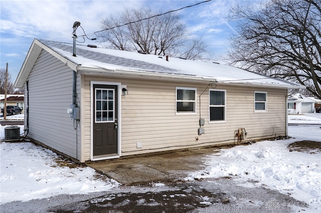 snow covered rear of property featuring central AC