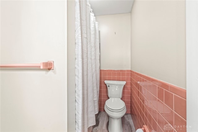 full bathroom with a wainscoted wall, toilet, wood finished floors, and tile walls