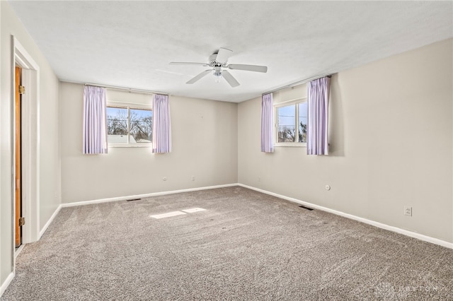 empty room featuring a wealth of natural light, carpet flooring, visible vents, and baseboards