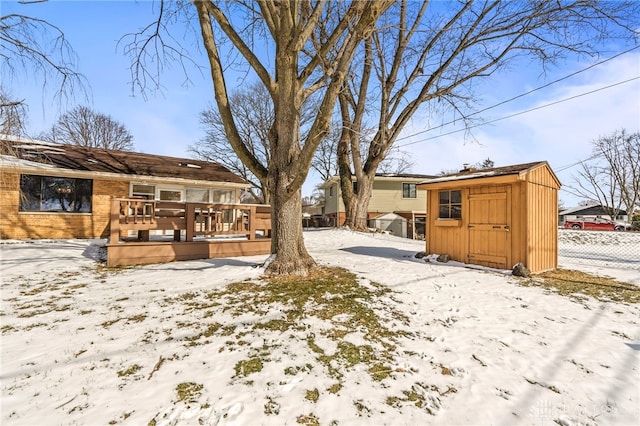 yard layered in snow with an outdoor structure, a deck, a storage shed, and fence