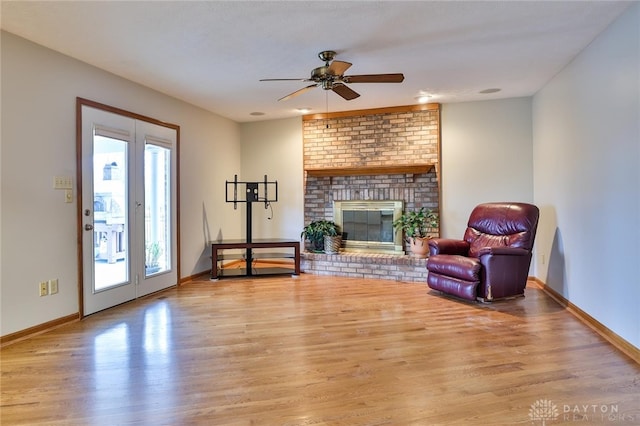 living area with light wood-type flooring, a fireplace, baseboards, and a ceiling fan