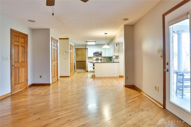 unfurnished living room with a ceiling fan, light wood-style flooring, and baseboards