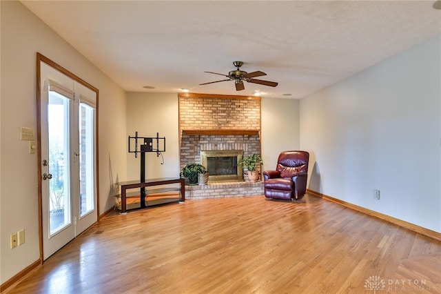 sitting room featuring light wood-style floors, ceiling fan, a fireplace, and baseboards