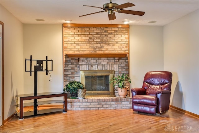 living area featuring ceiling fan, a brick fireplace, wood finished floors, and baseboards