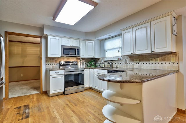 kitchen featuring dark stone counters, decorative backsplash, appliances with stainless steel finishes, a peninsula, and white cabinetry