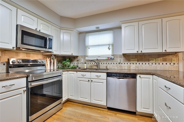 kitchen featuring light wood-style flooring, appliances with stainless steel finishes, white cabinetry, a sink, and dark stone counters