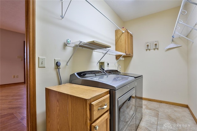 washroom featuring washing machine and clothes dryer, cabinet space, and baseboards